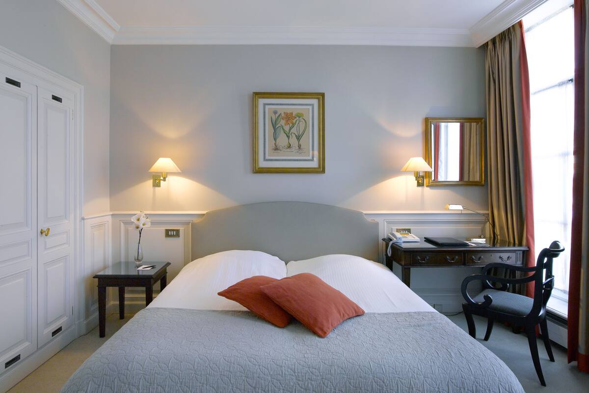 Hotelkamer met een groot bed, twee nachtkastjes, een bureau, een stoel, een spiegel en twee wandlampen.