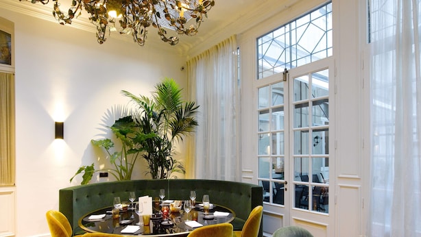 A dining area with a round table, yellow chairs, and a green upholstered bench. - Hotel Damier (Kortrijk)