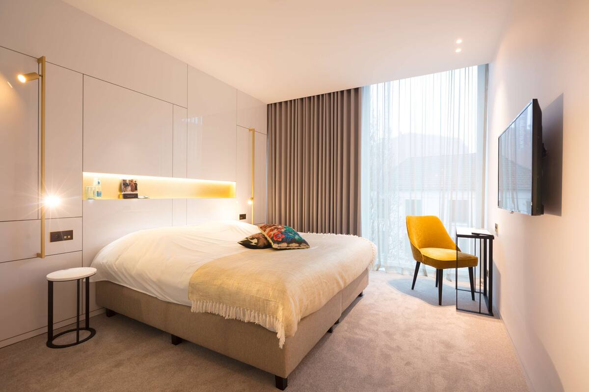 Een moderne hotelkamer met een groot bed, een tafeltje, een stoel en een aan de muur bevestigde televisie.