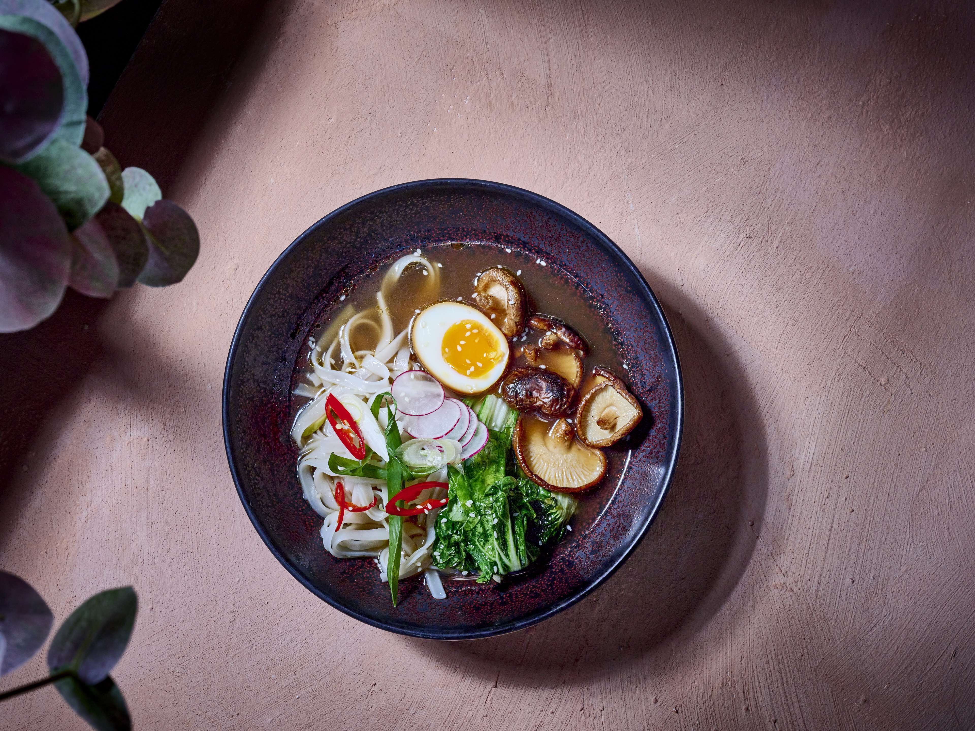 Un tazón de ramen con varios ingredientes como fideos, huevo, hongos y verduras.