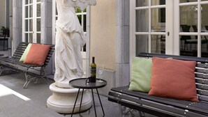 A statue of an angel on a pedestal, a bottle of wine, and two benches with cushions. - Hotel Damier (Kortrijk)