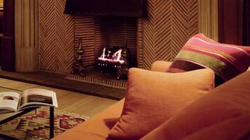 A cozy room with a fireplace, a painting of dogs, and a lamp.