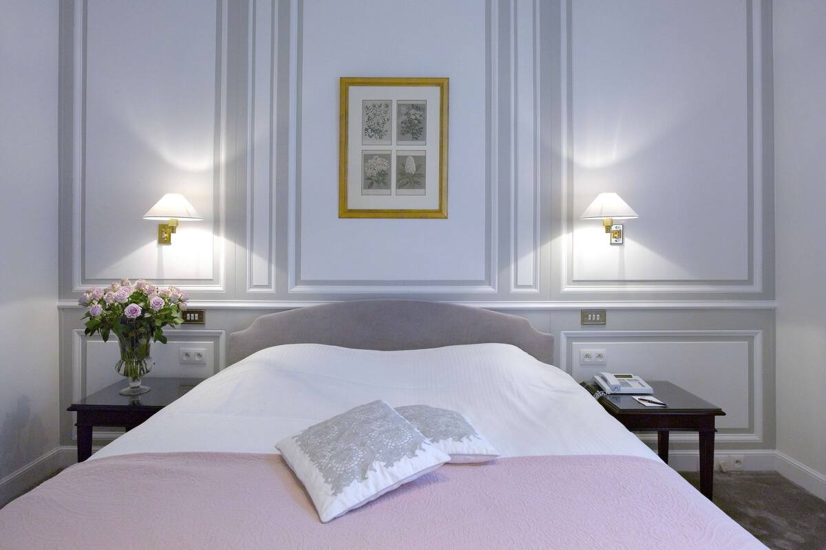 Een hotelkamer met een groot bed, twee nachtkastjes, een bloemenvaas en een ingelijste foto aan de muur.