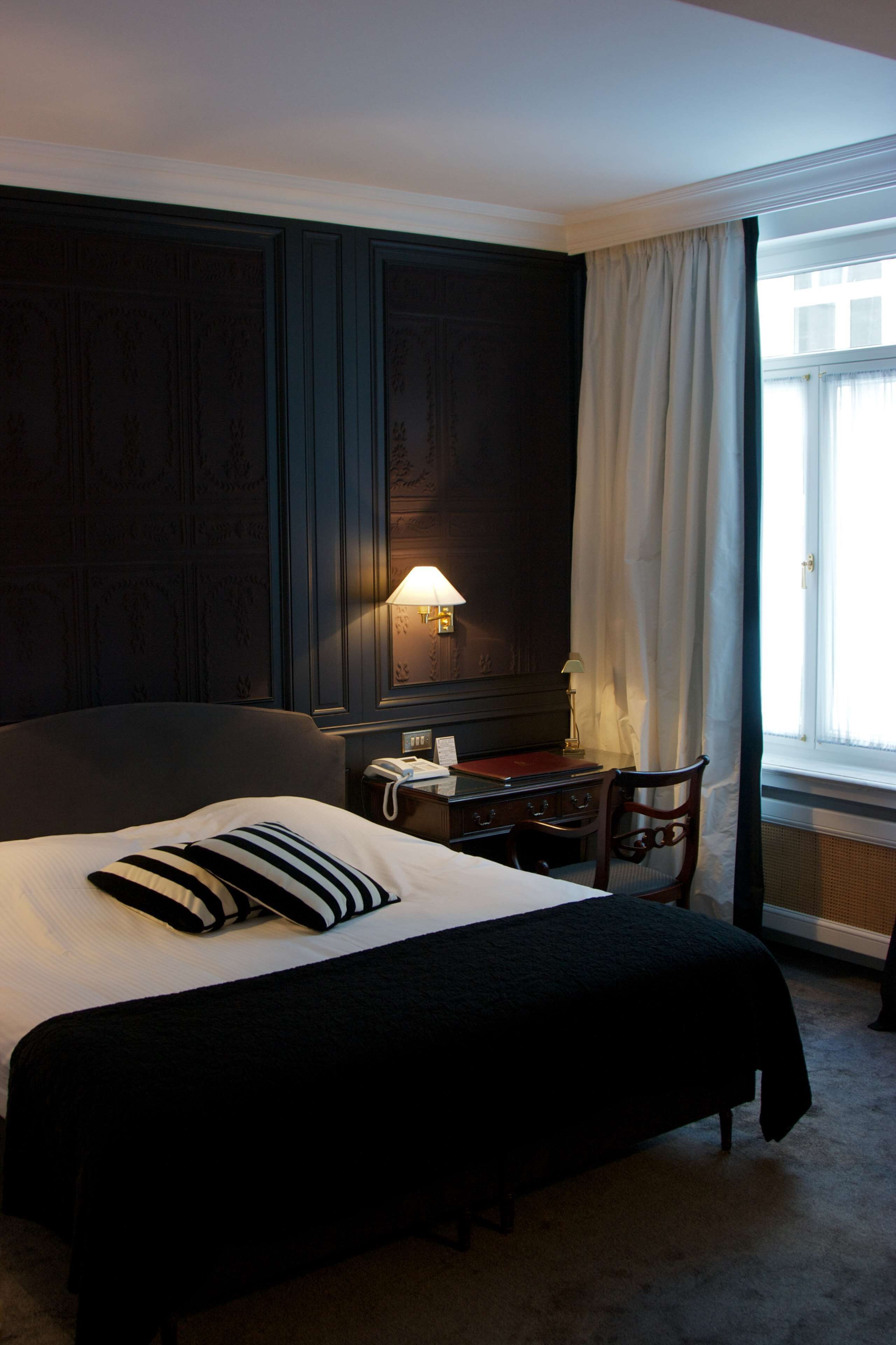 Una habitación de hotel con una cama grande, un escritorio, una silla, una lámpara y una ventana con cortinas.