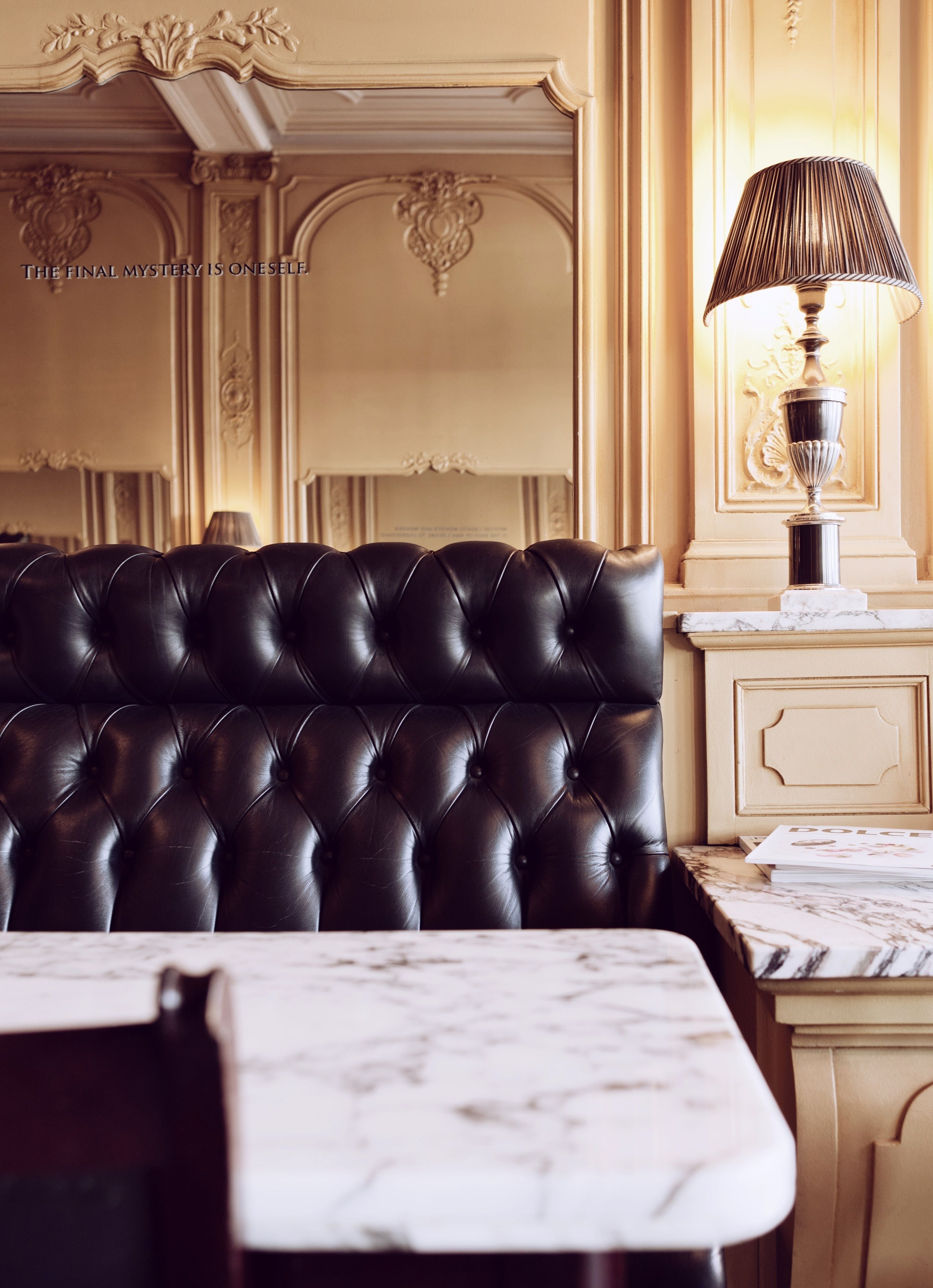 A black leather sofa with a marble table in front, a lamp, and a decorative wall with a plaque.