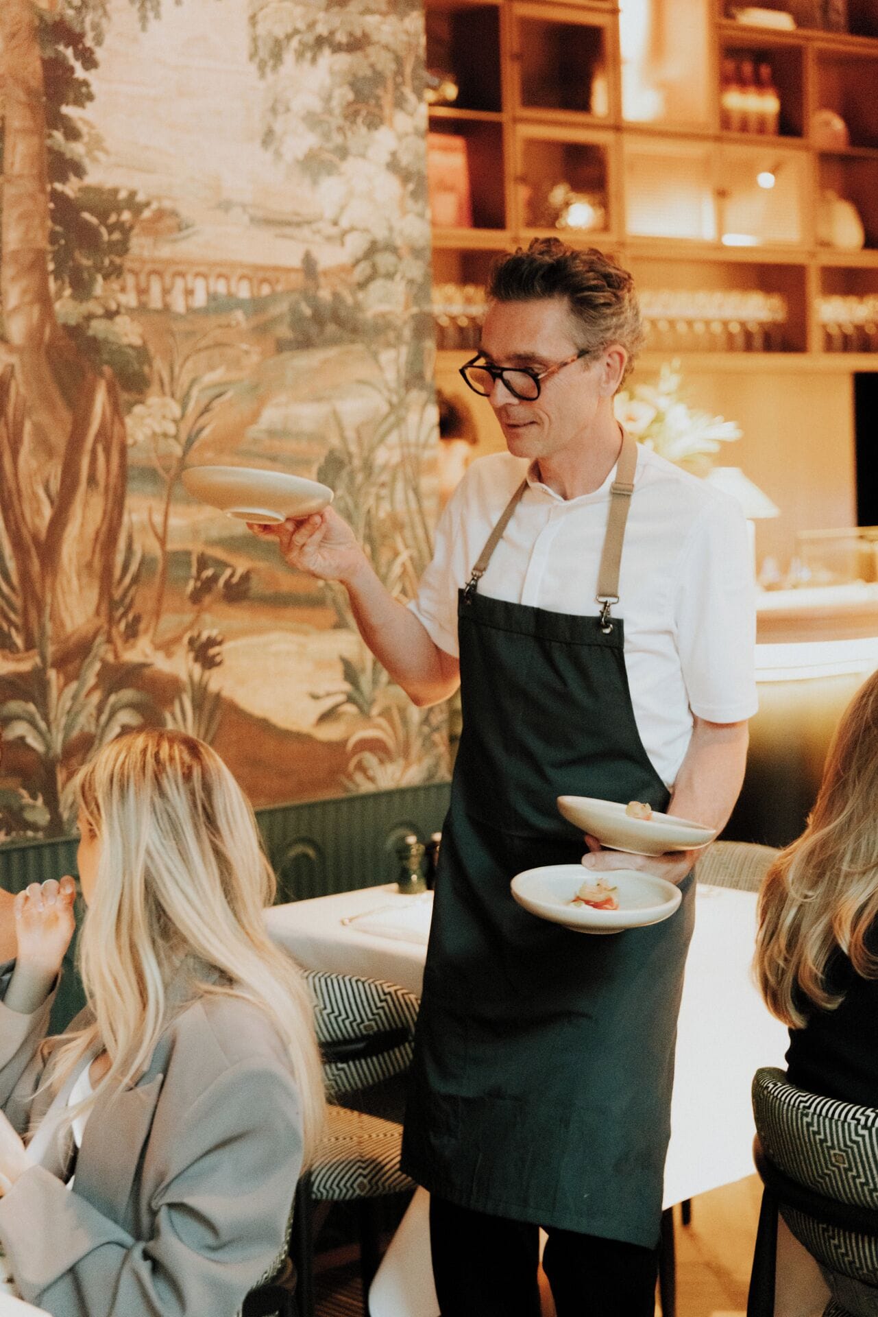 A waiter serving food in a restaurant with a mural on the wall.