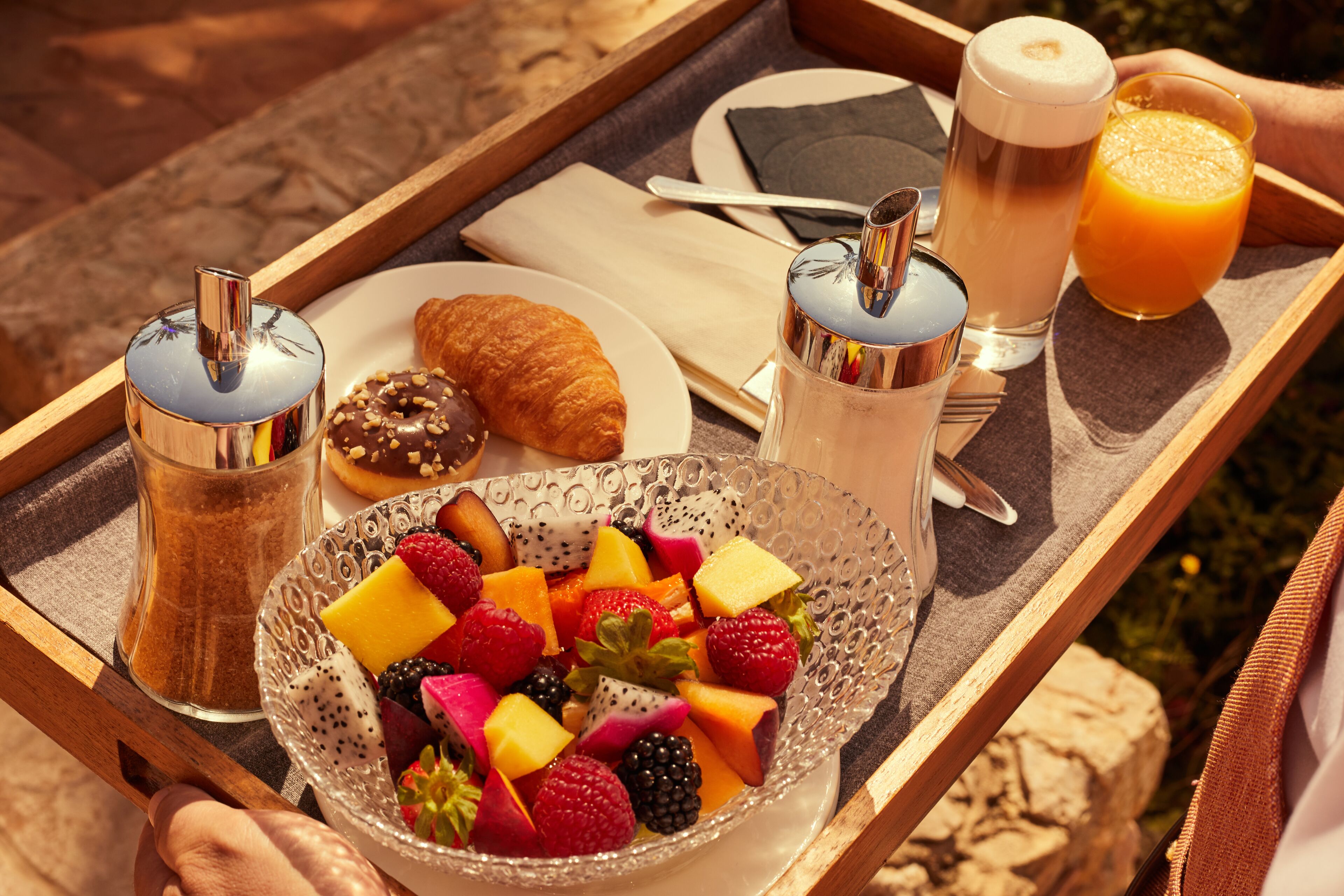 Ein Frühstücksbrett mit Croissant, Obstsalat, Kaffee und Orangensaft.