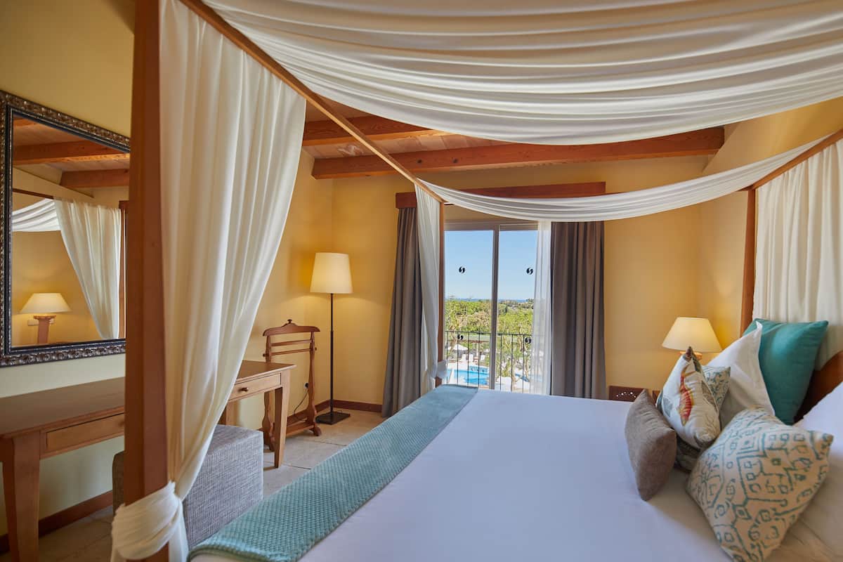 A hotel room with a bed, a desk, a chair, and a balcony with a pool view.