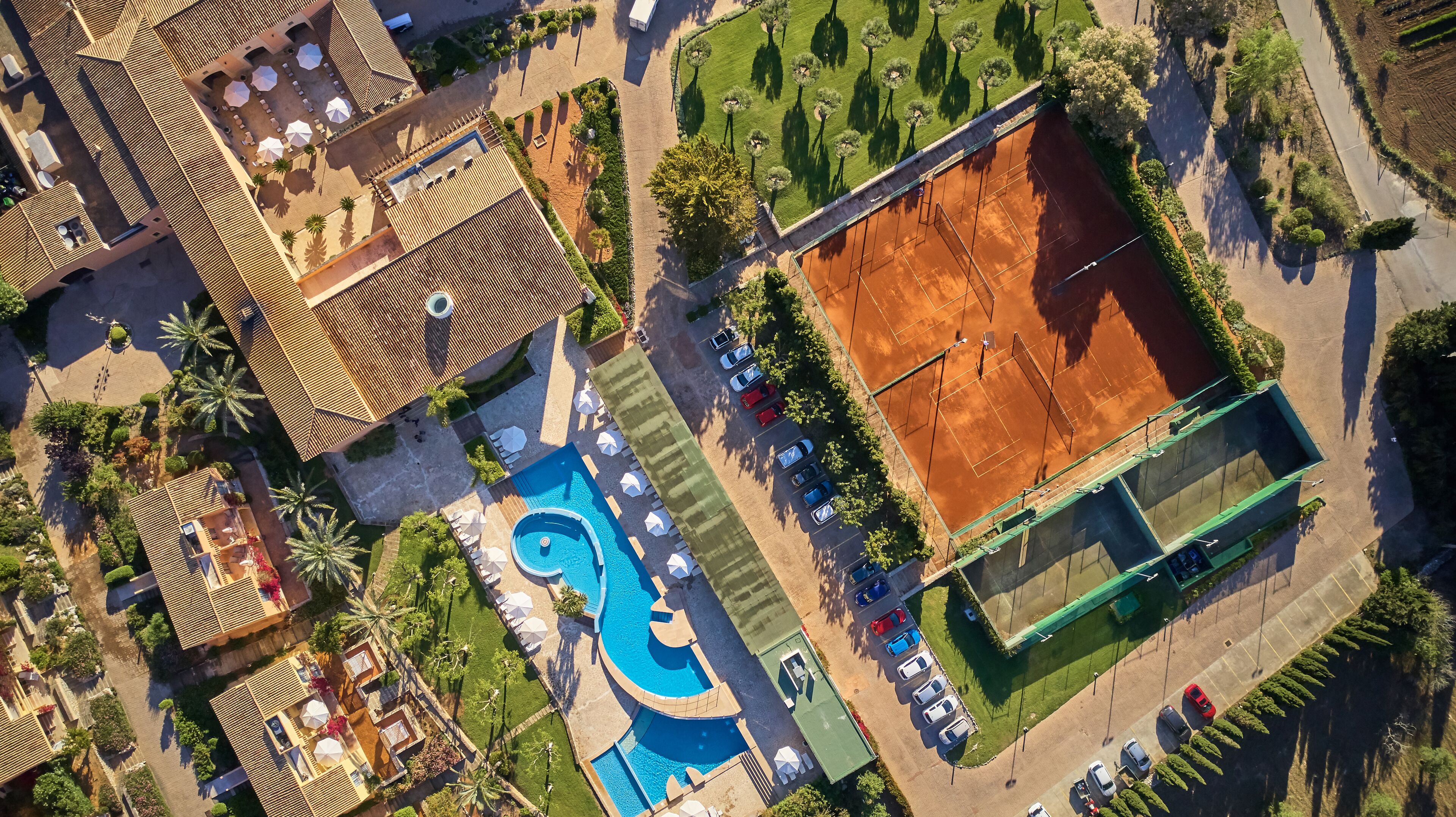 An aerial view of a resort with a swimming pool, tennis courts, and a parking area.