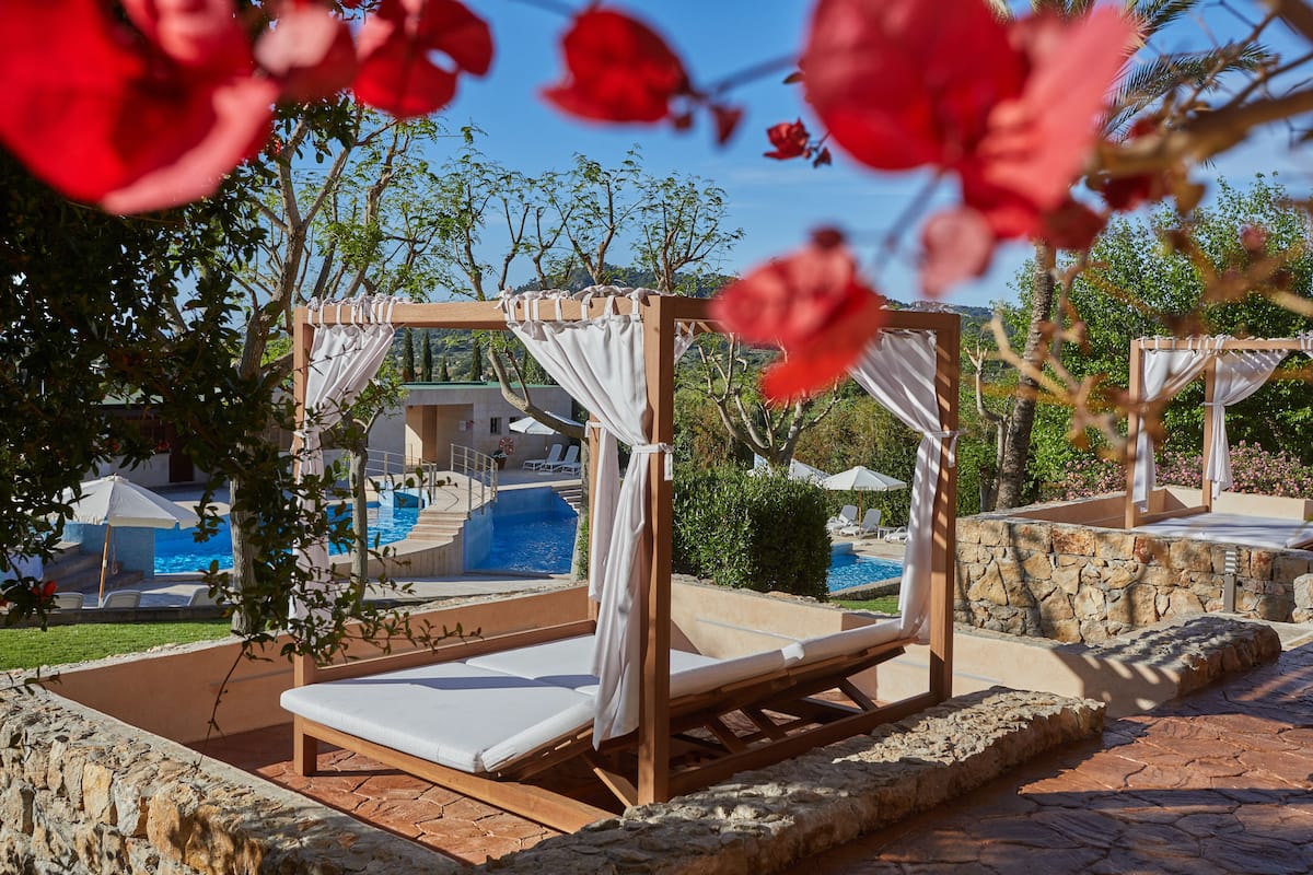 A poolside area with wooden cabanas, a swimming pool, and a stone wall.