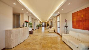 A hotel lobby with a reception desk, seating area, potted plants, and a large abstract painting on the wall. - Pula Suites Boutique Resort (Son Servera)