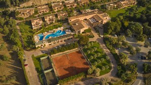 An aerial view of a resort with multiple buildings, a swimming pool, tennis courts, and surrounding greenery. - Pula Suites Boutique Resort (Son Servera)