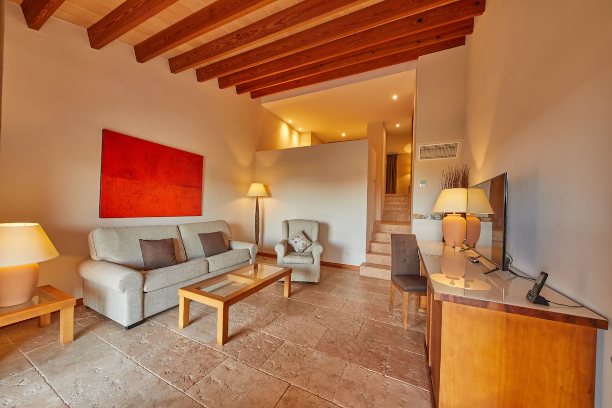 A modern living room with a sofa, armchairs, a coffee table, and a desk with a lamp and phone.