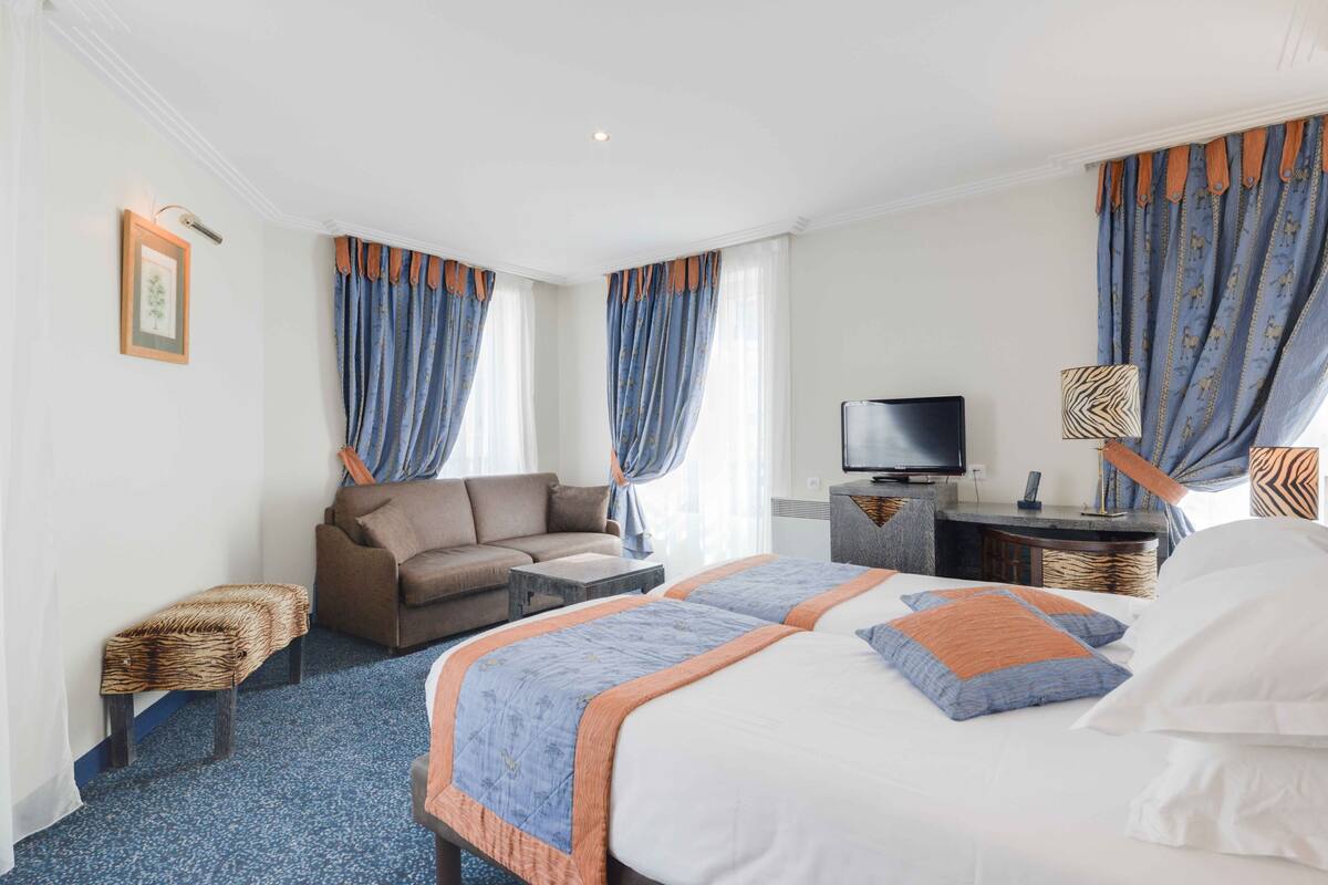 A hotel room with a bed, two bedside tables, a television, a sofa, and a small bench.