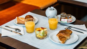 Une table dressée pour le petit-déjeuner, avec des croissants, des fruits, du jus et des pots de miel.