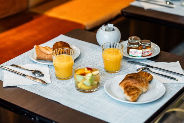 A breakfast setup with croissants, fruit, juice, and honey jars on a table. - Pavillon Opera Grands Boulevards (Paris)