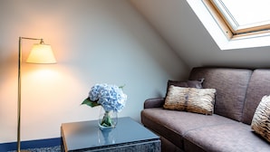 A modern living room with a sofa, a side table with a vase of flowers, a floor lamp, and a skylight.
