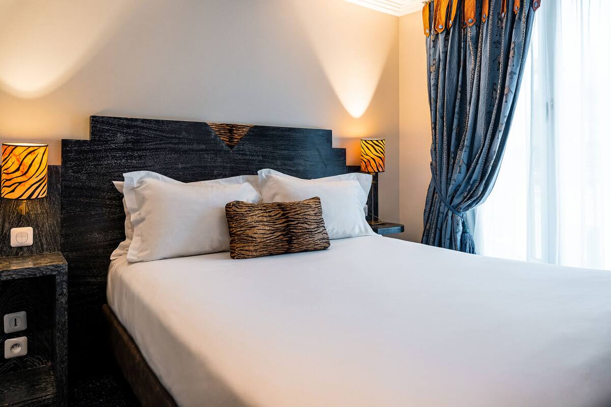 A neatly made bed with white and patterned pillows, a dark headboard, and two wall-mounted lamps with tiger-striped shades.
