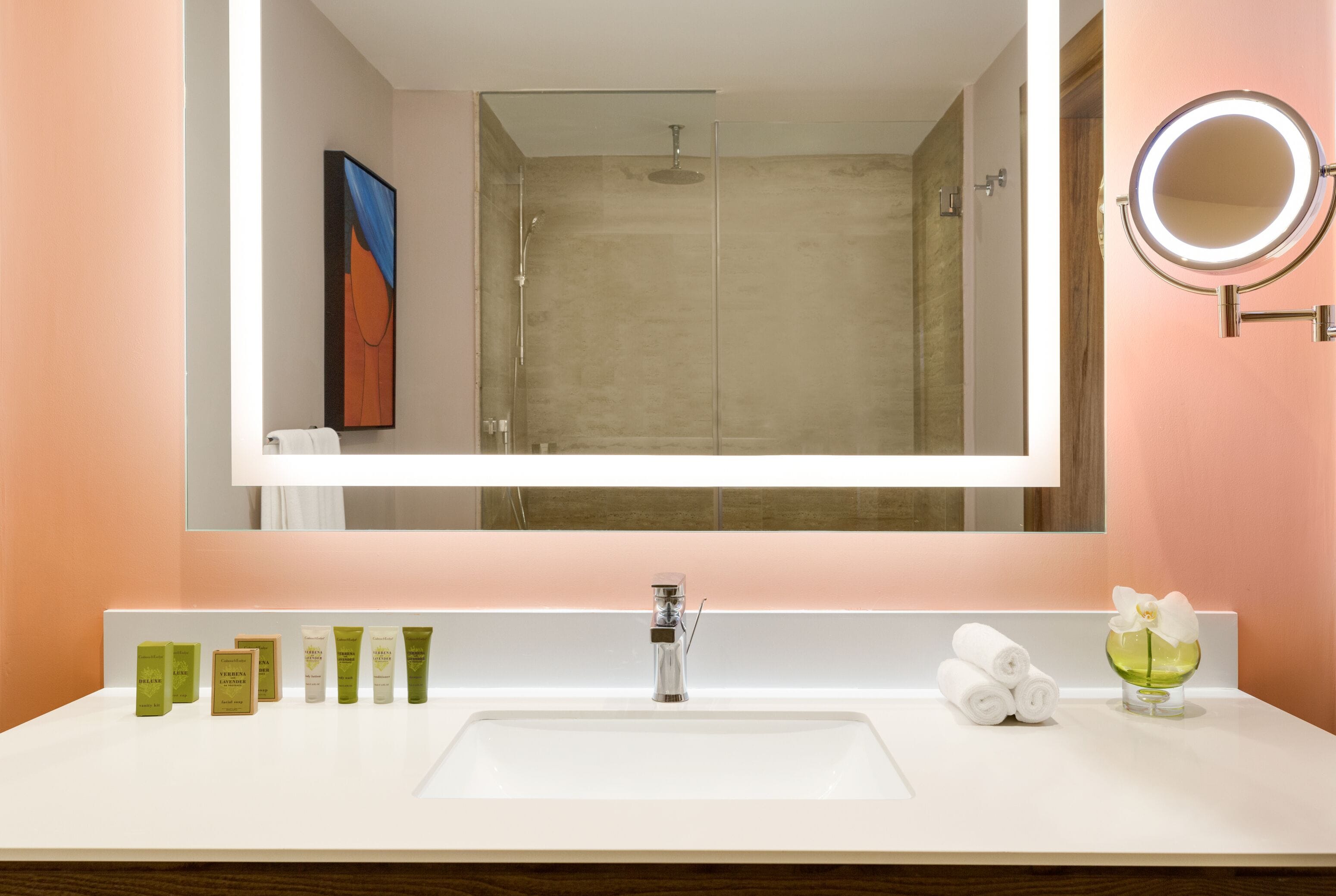 Un baño con un espejo grande, un lavabo y una ducha. Hay artículos de tocador en la encimera.