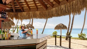 A bar with a view of the ocean, surrounded by palm trees and a thatched roof. - Dreams La Romana Resort & Spa - All Inclusive (San Rafael del Yuma)