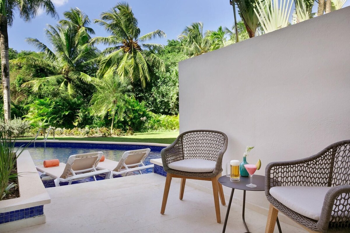 A poolside area with lounge chairs, a small table, and a view of a tropical garden.