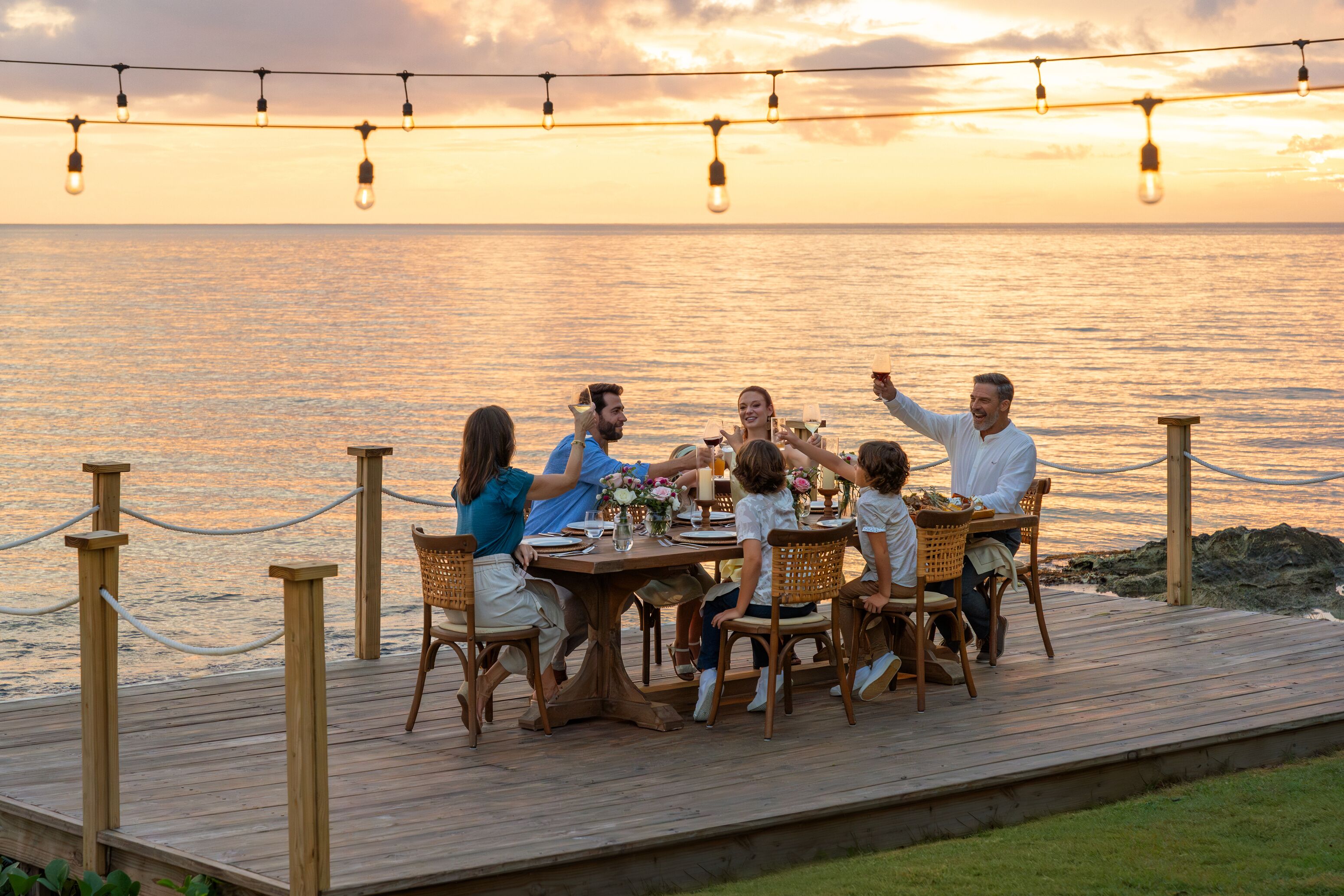 Une terrasse en bois avec une table dressée pour accueillir un groupe de personnes qui savourent un repas en bord de mer.