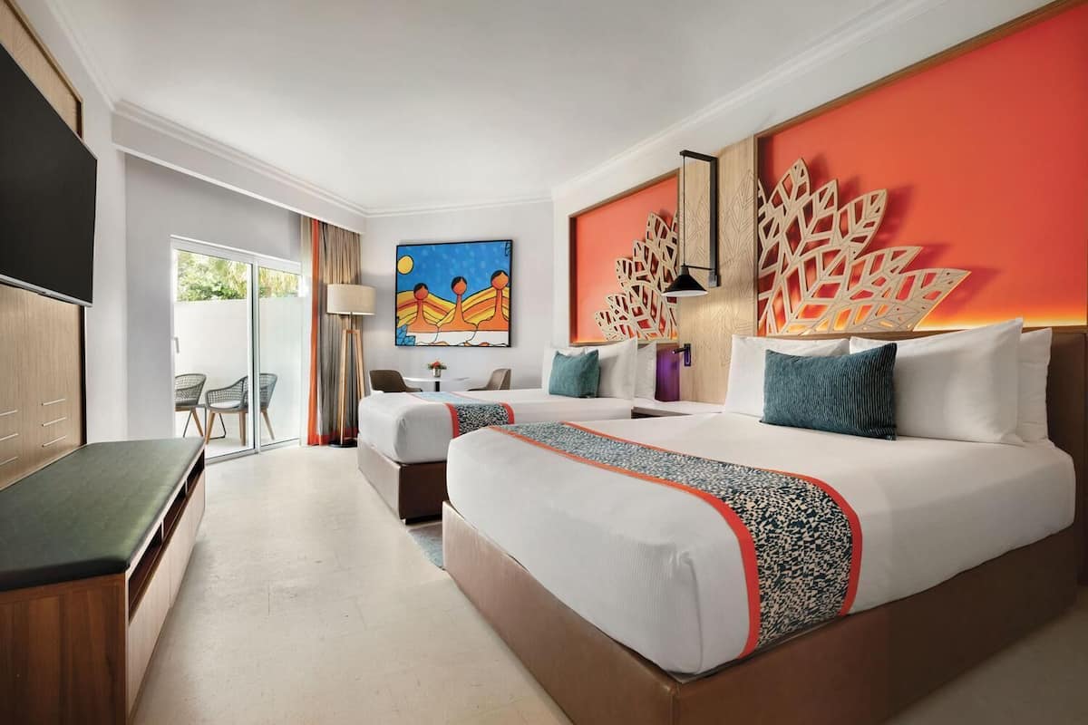 A hotel room with a large bed, a smaller bed, a desk, and a chair. There is a painting on the wall and a decorative wall panel.
