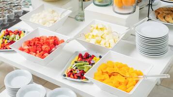 Una mesa de buffet con diversas opciones de fruta y platos blancos apilados.