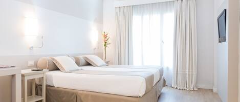 A hotel room with two beds, a desk, a TV, and a window with curtains.