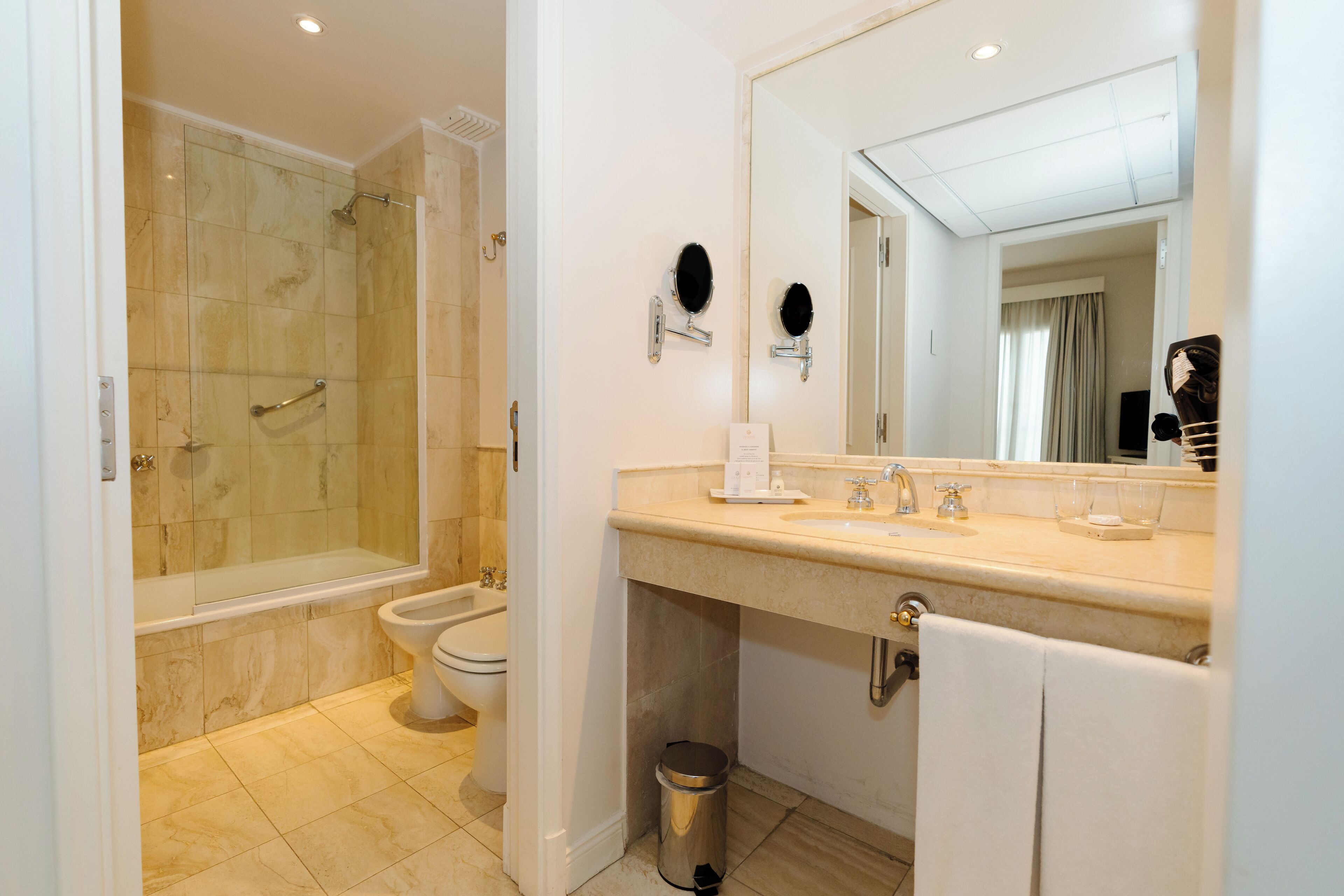 Un baño moderno con ducha a ras de suelo, un bidé, un espejo grande y un tocador con un perchero para toallas.