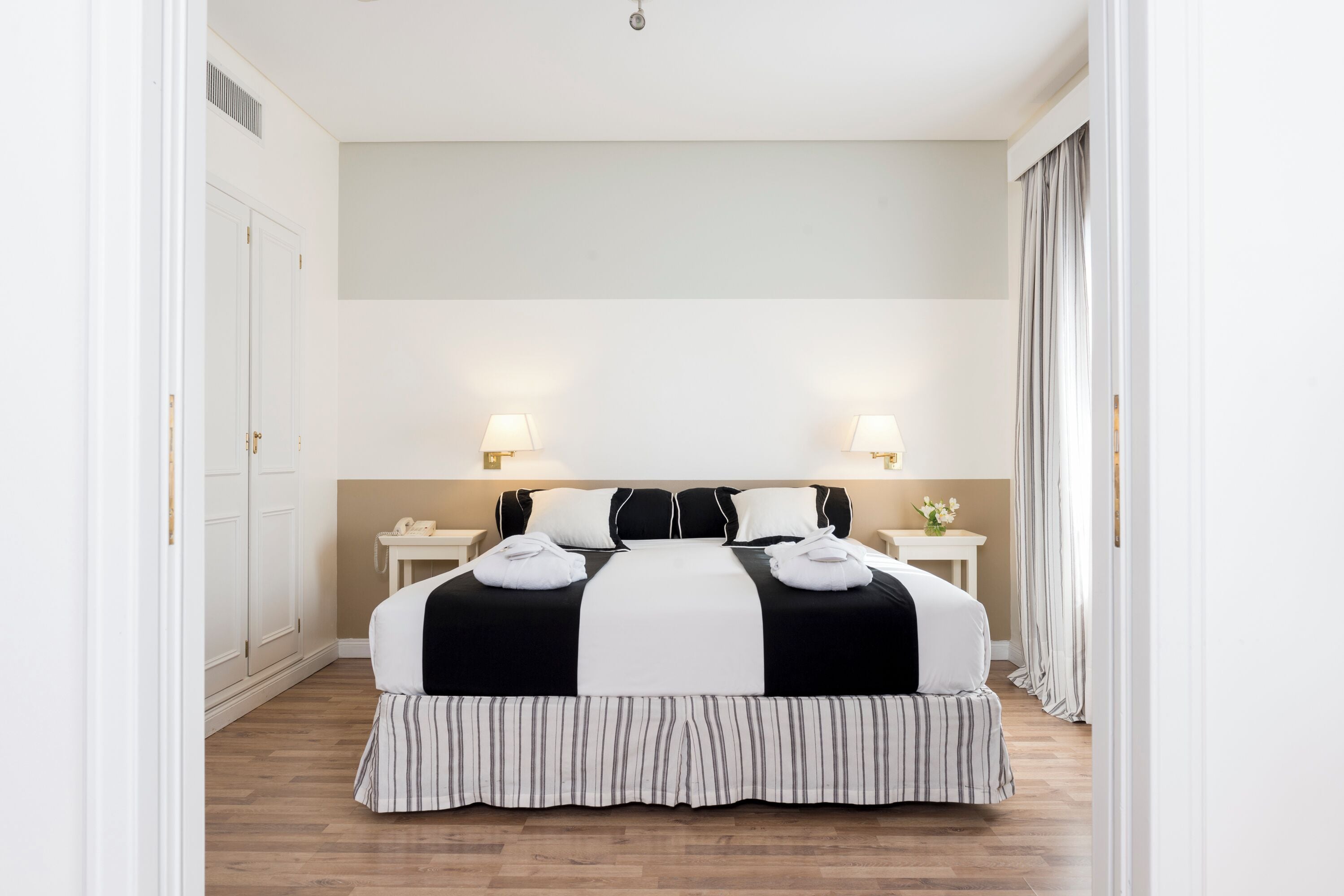 Quarto de hotel com uma cama grande, duas mesas de cabeceira e um criado-mudo.