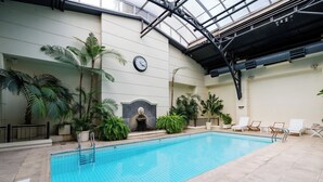 Ein Hallenbad mit gefliesten Wänden, einer Uhr und Liegestühlen.