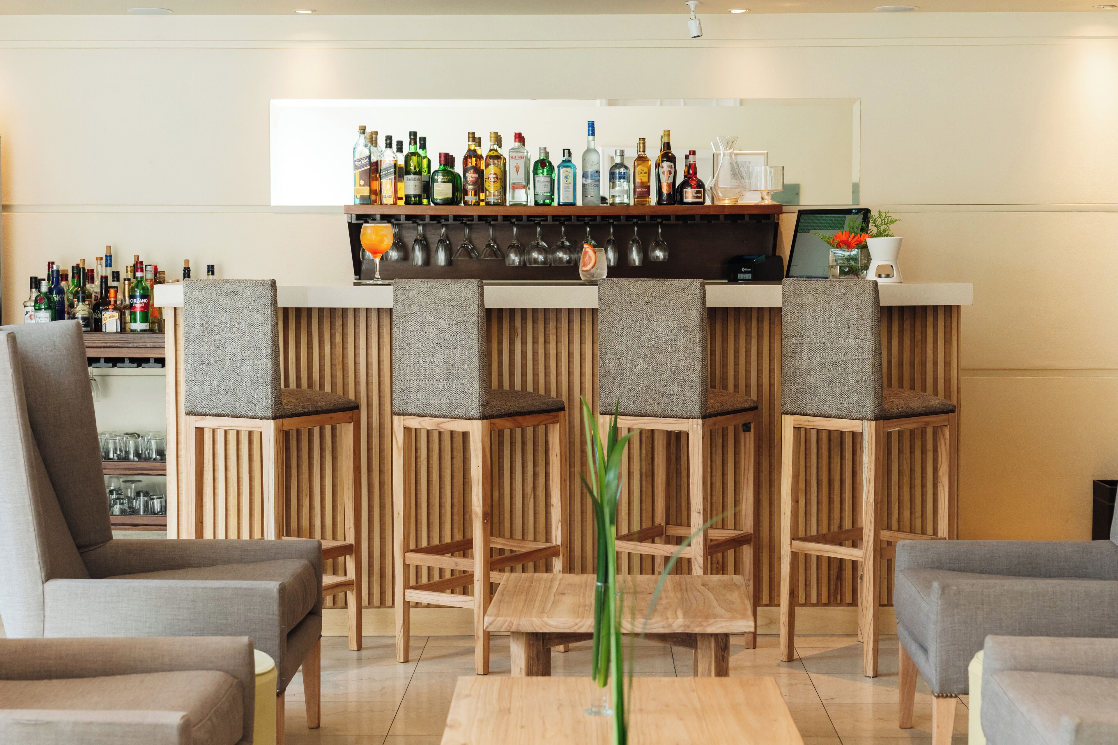 A bar area with multiple liquor bottles, a bar counter, and seating with cushioned chairs.