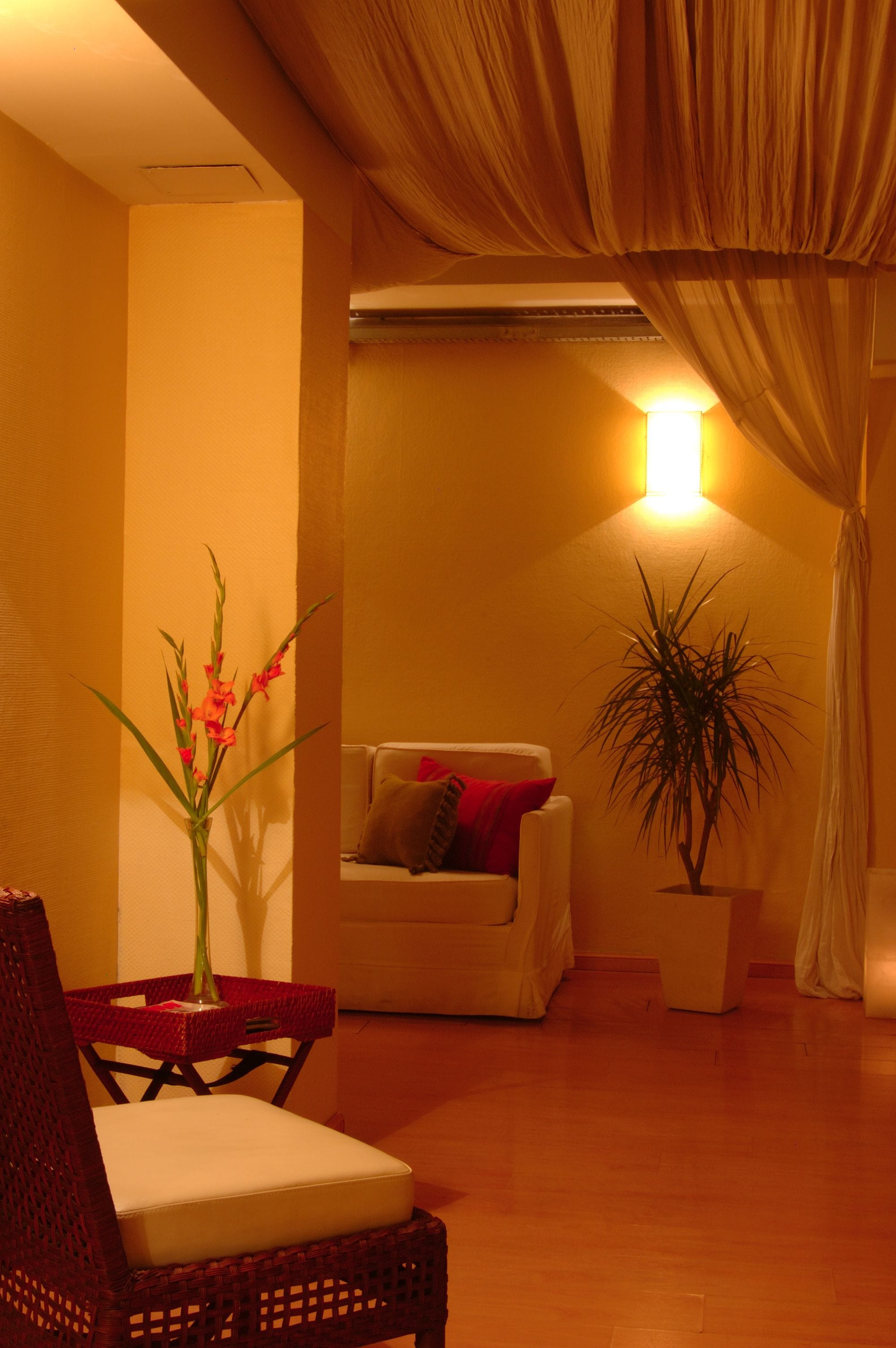 Una sala de estar acogedora con un sillón de mimbre, un sofá blanco, una planta en maceta y un jarrón con flores.