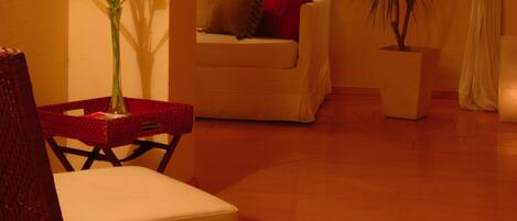 Una sala de estar acogedora con un sillón de mimbre, un sofá blanco, una planta en maceta y un jarrón con flores.