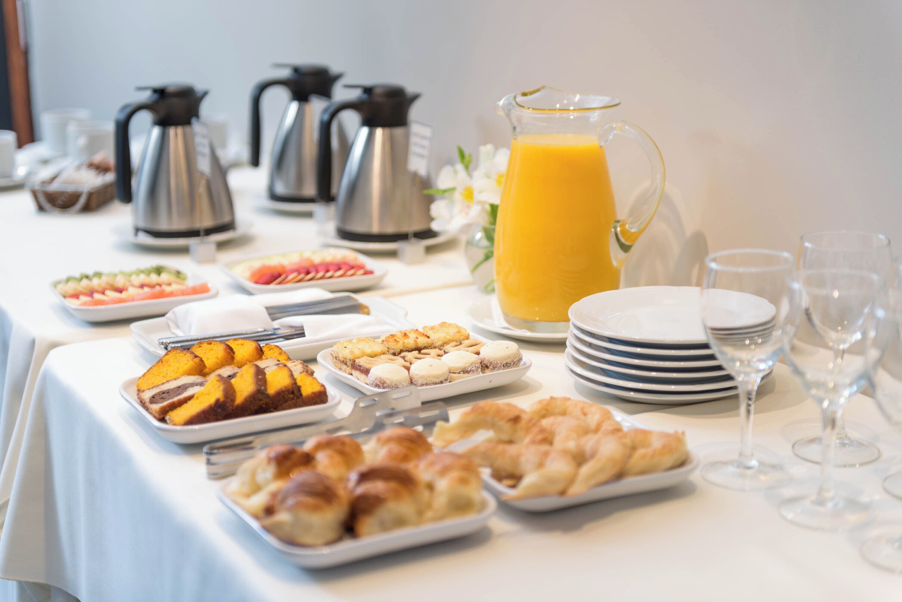 A breakfast buffet with various pastries, a pitcher of orange juice, and coffee pots.