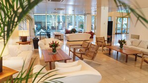 Eine großzügige Lobby mit weißen Möbeln, großen Fenstern und Blick ins Freie.