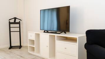 Una habitación con televisión sobre un mueble blanco, una silla negra y un perchero.
