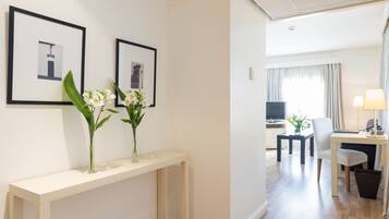 Habitación de hotel con una mesa consola blanca, dos cuadros enmarcados, un escritorio con silla, un televisor y una lámpara.
