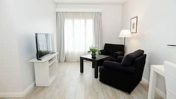 Een moderne woonkamer met een flatscreen televisie, een zwarte bank, een bijzettafeltje met een plant en een lamp.