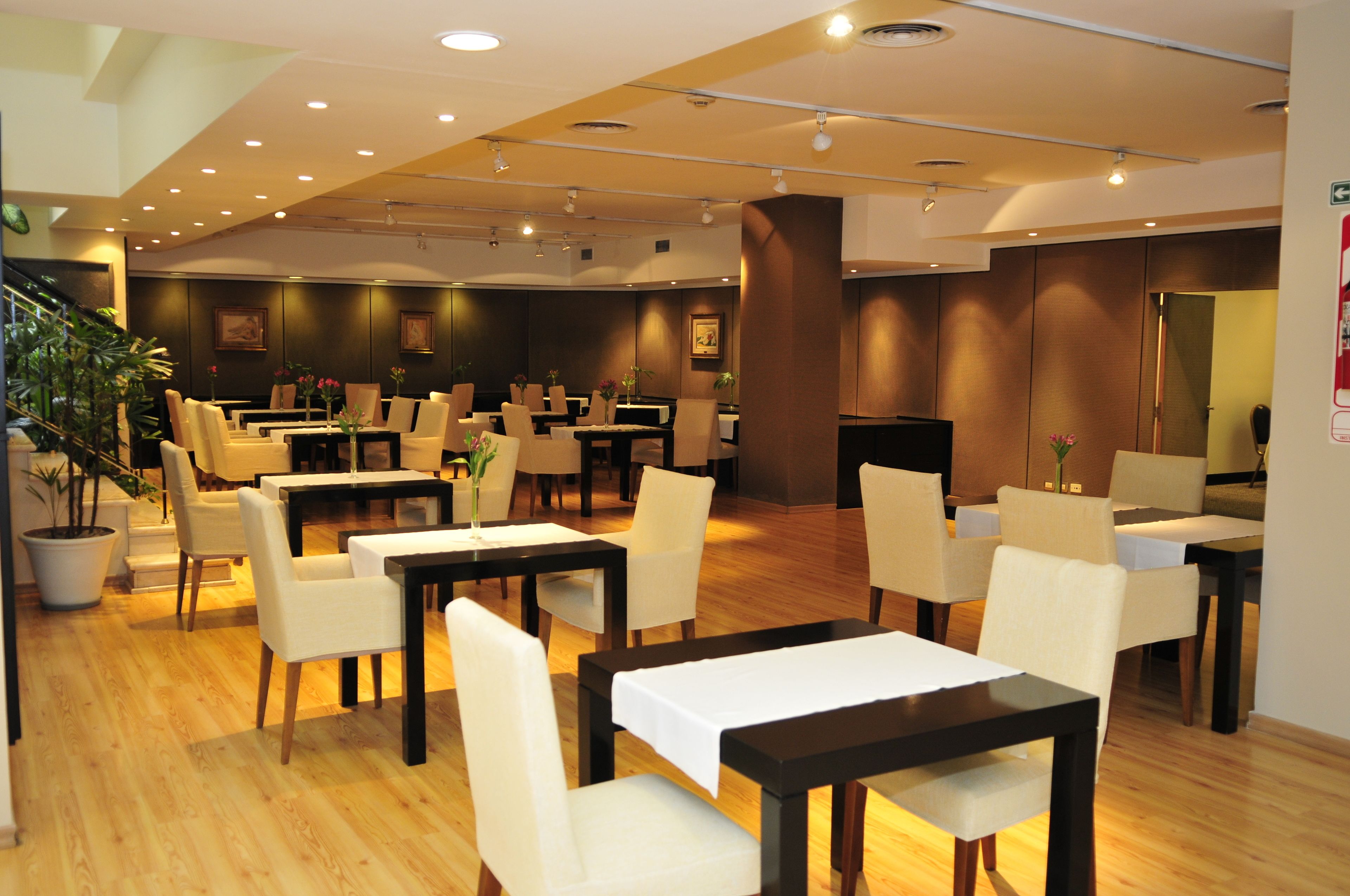 Ein geräumiges Restaurant mit mehreren Tischen und Stühlen, Holzboden und Einbaustrahler.