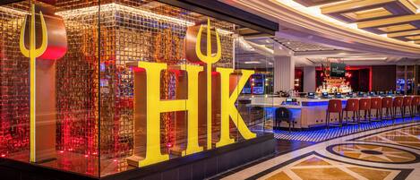 Un espace bar moderne, agrémenté d’un grand panneau lumineux avec les initiales « HK », d’un plafond bien éclairé et d’un comptoir avec des places assises.