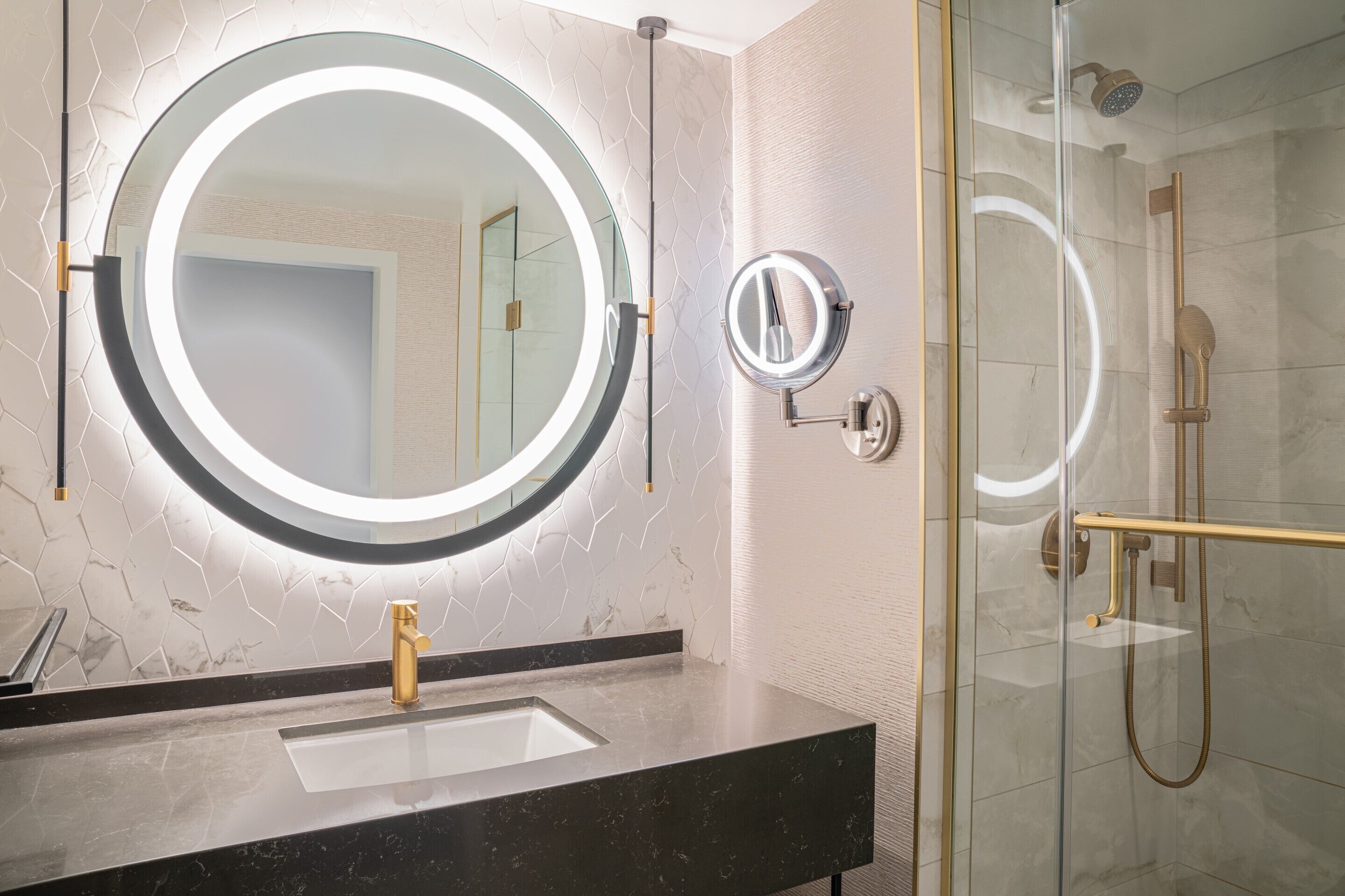 Une salle de bain avec un miroir rond, un robinet doré et une douche séparée par des parois en verre.