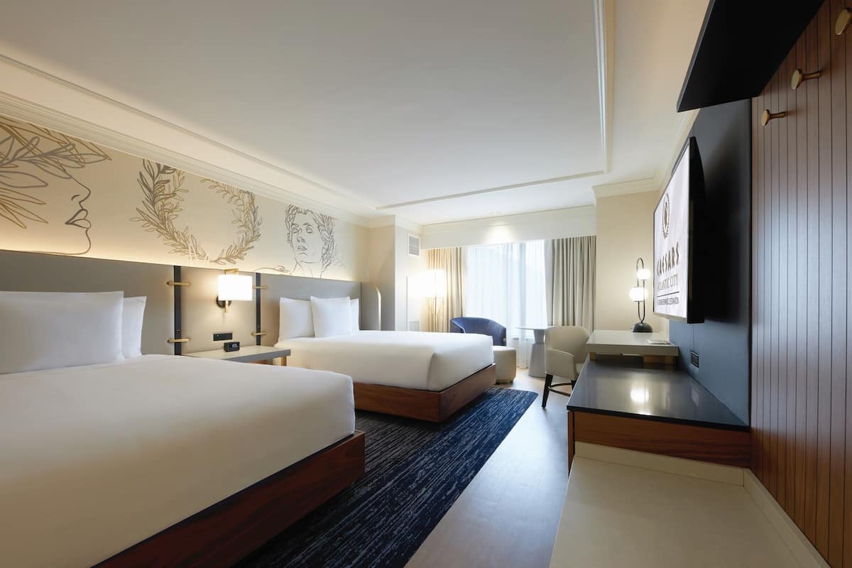Ein Hotelzimmer mit zwei Betten, einem Schreibtisch, einem Stuhl, einem Fernseher und einer Wand mit dekorativem Design.