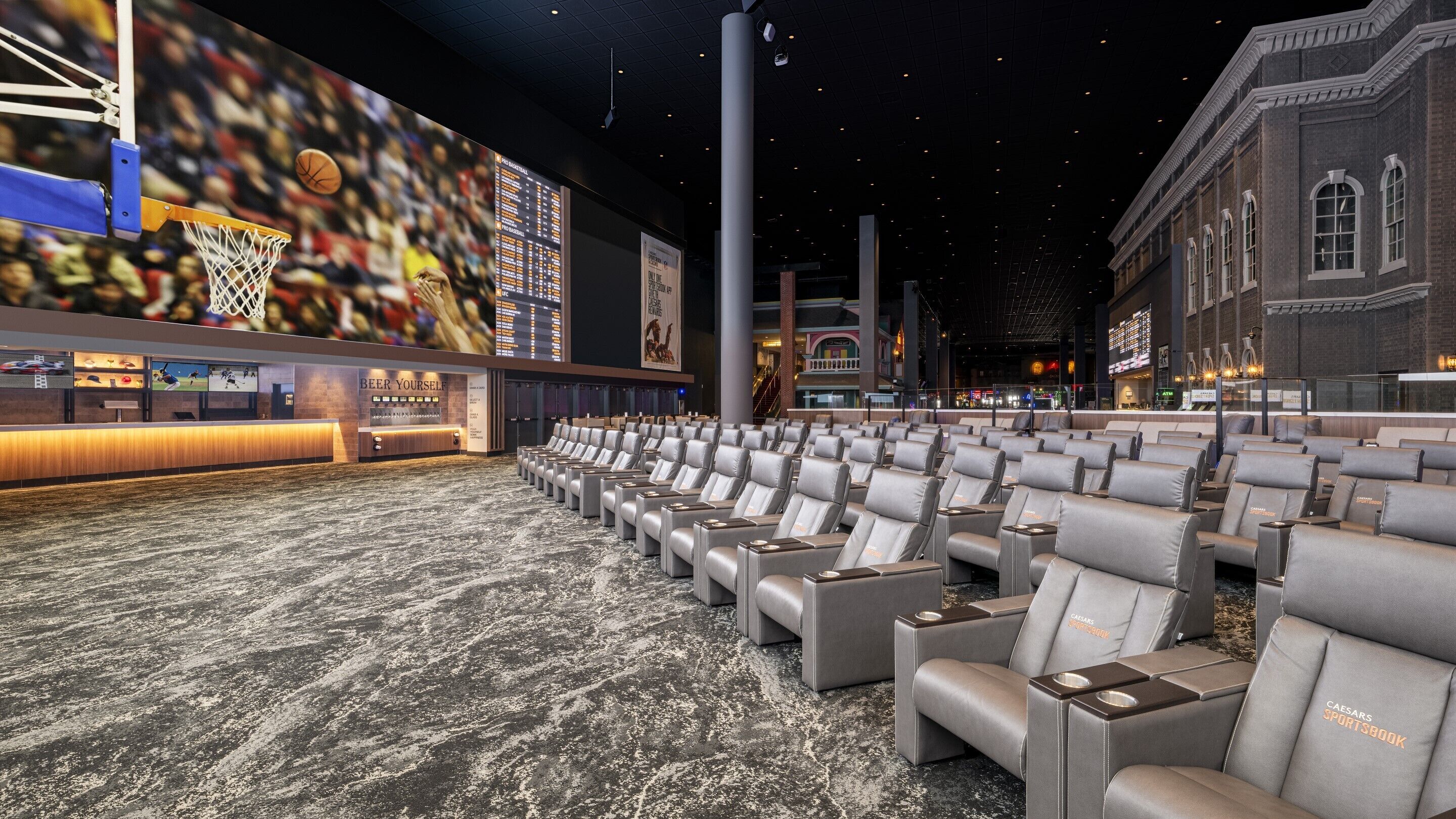A spacious indoor area with rows of seating, a reception desk, and a large screen displaying sports content.