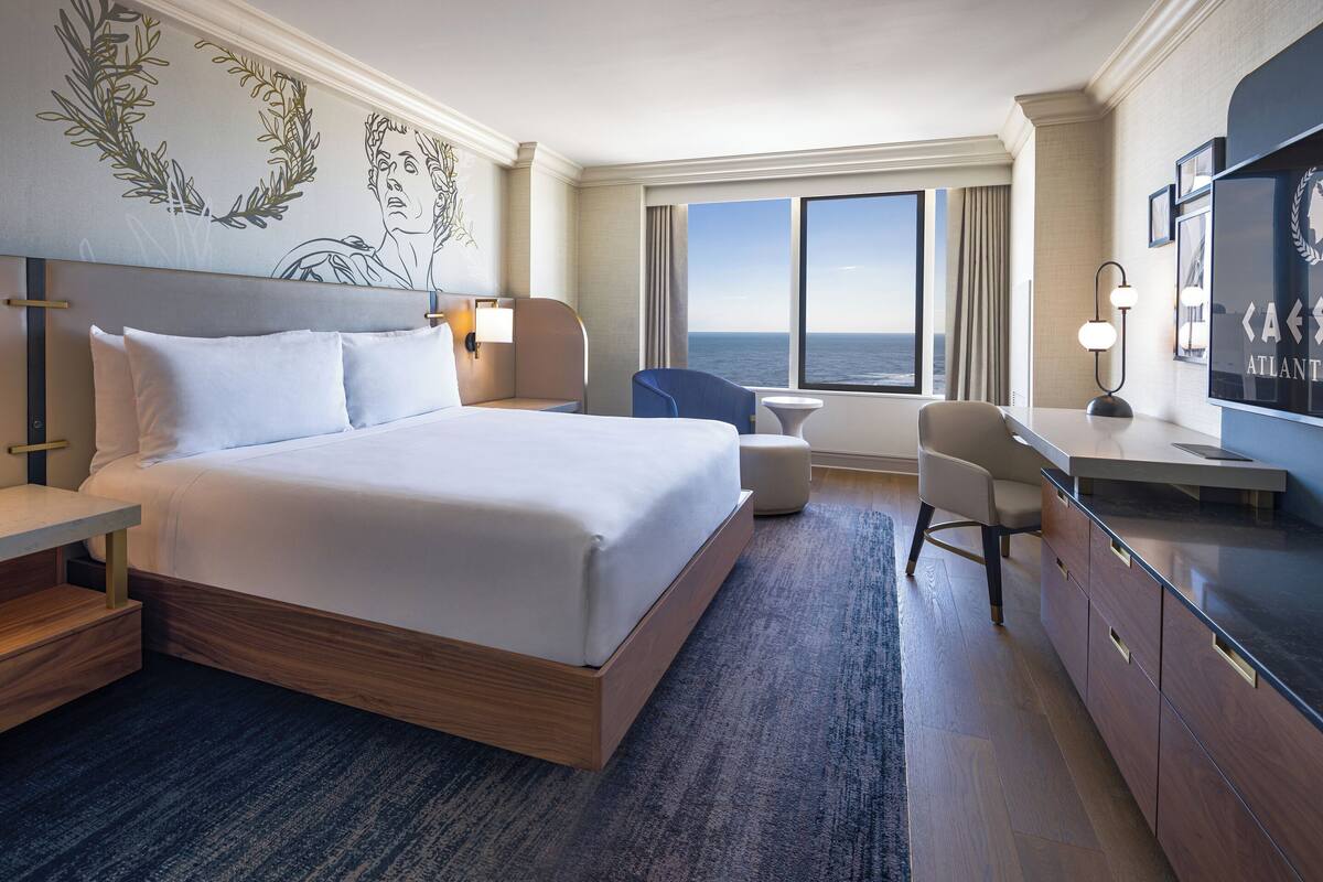 Ein Hotelzimmer mit einem großen Bett, einem Schreibtisch, einem Sessel, einem Fernseher und Blick aufs Meer.