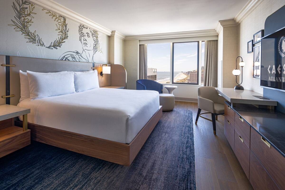 Ein Hotelzimmer mit einem großen Bett, einem Schreibtisch, einem Stuhl und Blick auf die Stadt.