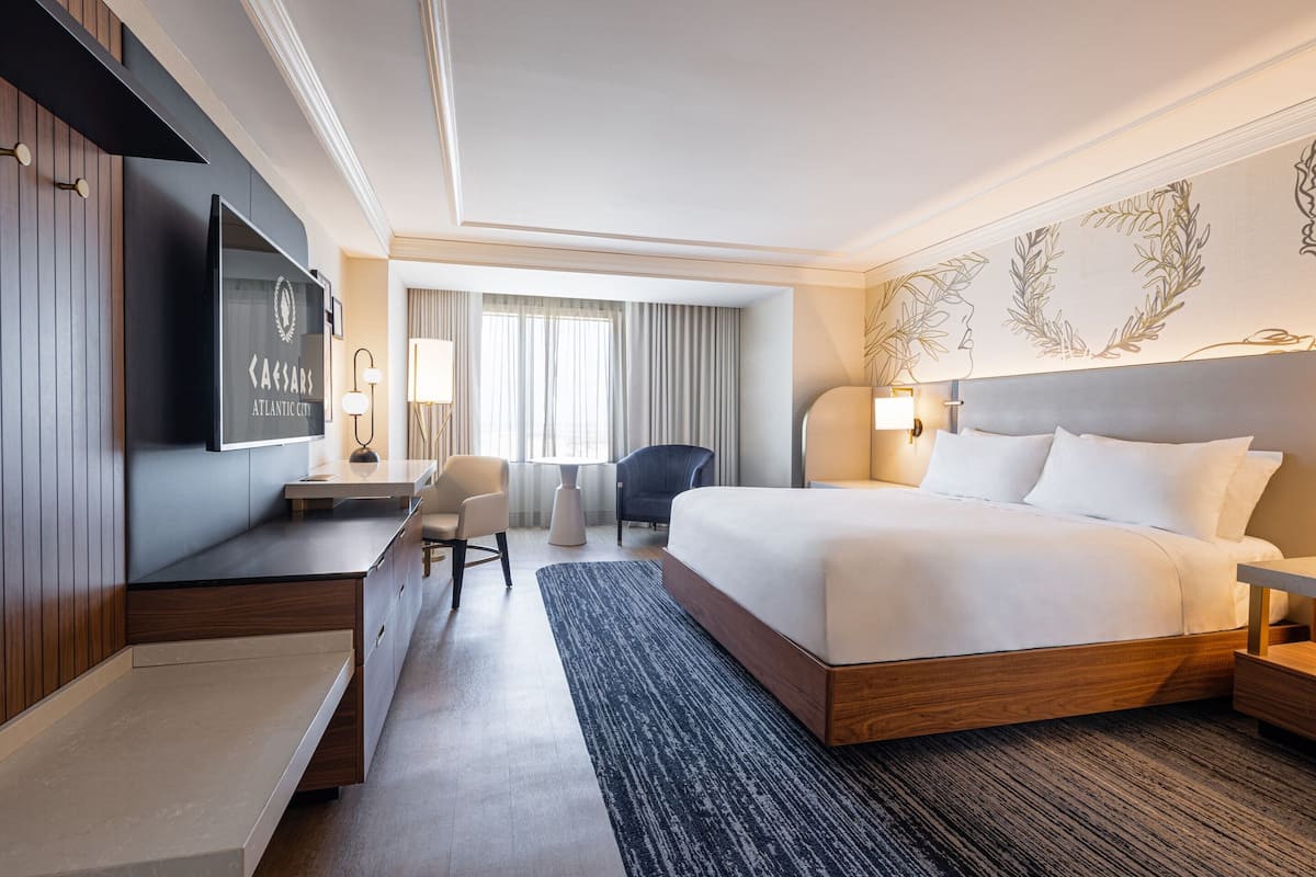 Ein modernes Hotelzimmer mit einem großen Bett, einem Schreibtisch, einem Stuhl und einem Fernseher, der den Namen des Hotels zeigt.