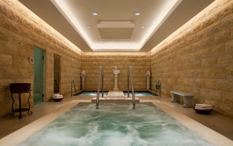 A spa area with a large hot tub, stone walls, and a ceiling with recessed lighting.