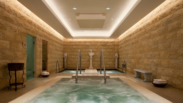 A spa area with a large hot tub, stone walls, and a ceiling with recessed lighting.
